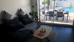 A living room with a sofa, a coffee table, and a view of an outdoor pool area. - Maison Vallée: Swimming Pool / Groupama Stadium / Euroexpo / LDLC ARENA / Access to Downtown (Décines-Charpieu)