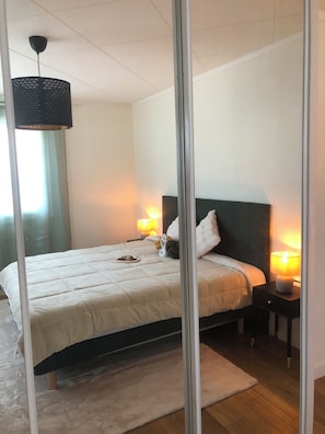 A bedroom with a bed, bedside lamps, a mirror, and a hanging light fixture.