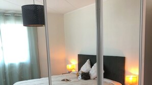 A bedroom with a bed, bedside lamps, a nightstand, a mirror, and a hanging light fixture. - Maison Vallée: Swimming Pool / Groupama Stadium / Euroexpo / LDLC ARENA / Access to Downtown (Décines-Charpieu)