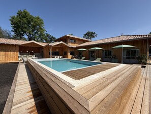 Eine Holzterrasse mit Pool, Sitzgelegenheiten im Freien und einer überdachten Terrasse.