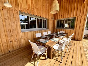 Eine Holzterrasse mit einem Esstisch, gedeckt für vier Personen, umgeben von Korbstühlen.