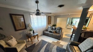 A living room with a sofa, armchair, and a coffee table. There is a ceiling fan, a window with curtains, and a door leading to another room. - Lakefront home located 10 minutes from the Hardrock Stadium for the World Cup (Miami)