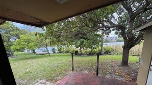 A covered patio area with a red floor, a blue folding chair, and a view of a grassy yard with trees and a body of water in the background. - Lakefront home located 10 minutes from the Hardrock Stadium for the World Cup (Miami)