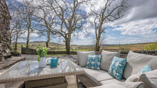 An outdoor seating area with a wicker table, cushions, and a view of the countryside. - Braich-Y-Big -  a self catering cottage that sleeps 5 guests  in 3 bedrooms (Garndolbenmaen)