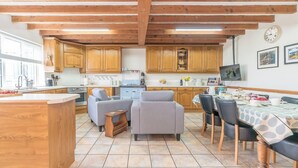 A kitchen with wooden cabinets, a dining area with a table and chairs, and a kitchen island. - Braich-Y-Big -  a self catering cottage that sleeps 5 guests  in 3 bedrooms (Garndolbenmaen)