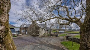 A stone house with a gravel driveway, a stone wall, and a grassy area with a view of hills. - Braich-Y-Big -  a self catering cottage that sleeps 5 guests  in 3 bedrooms (Garndolbenmaen)