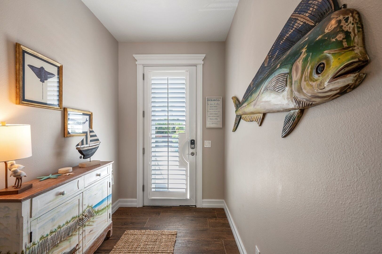 A hallway with a wooden dresser, a framed picture, a lamp, and a large fish mural on the wall.