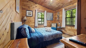 Una habitación tipo cabaña de madera con una cama, una silla, una mesa y un ventilador de techo.