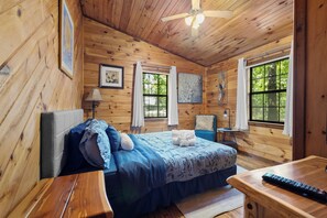 Una habitación tipo cabaña de madera con una cama, una silla, una mesa y un ventilador de techo.
