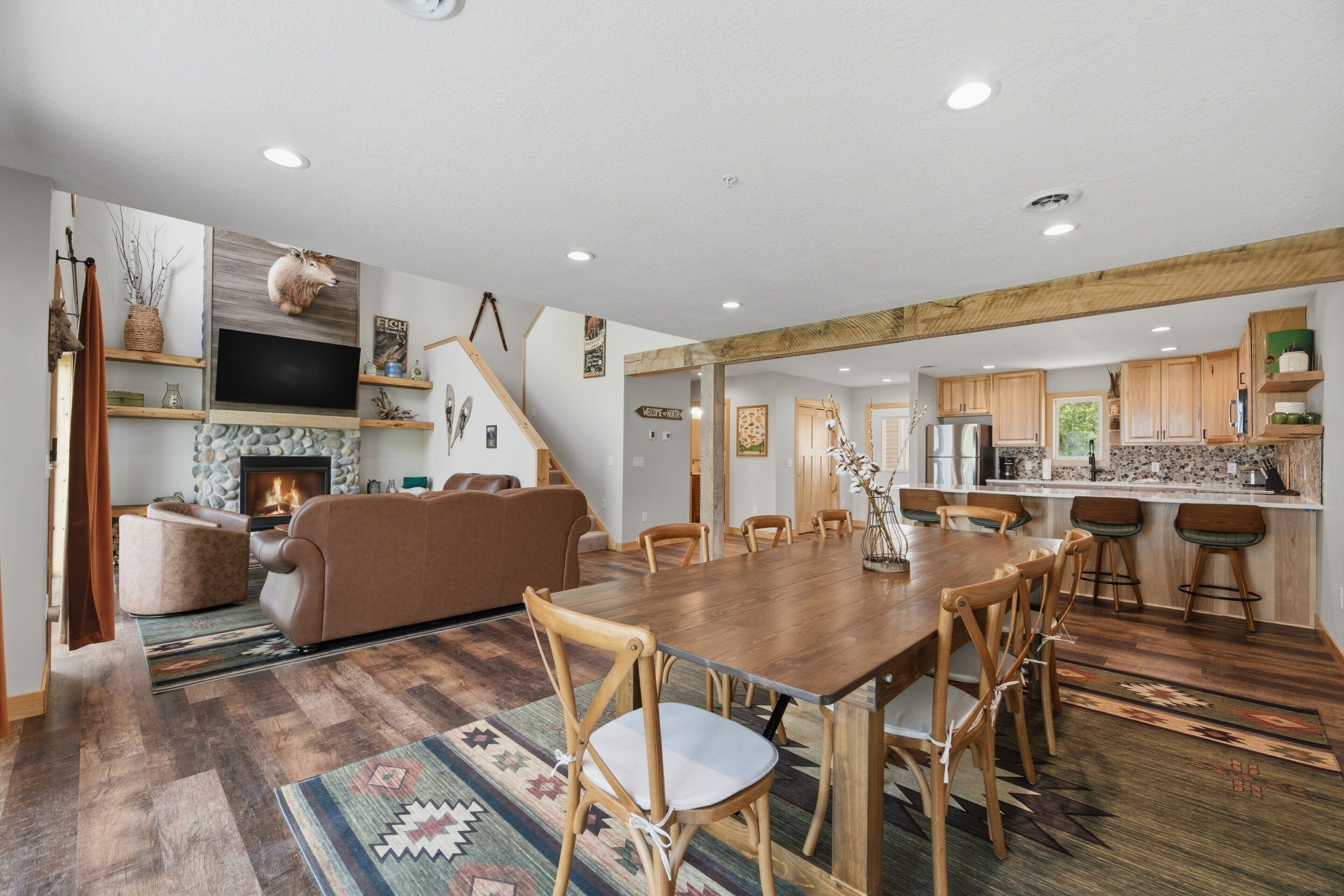 A spacious living area with a fireplace, wooden dining table, and a kitchen with wooden cabinets.