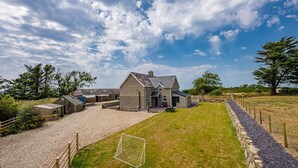 A house with a gravel driveway, a grassy lawn, and a stone wall.