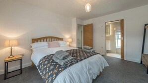 A bedroom with a bed, bedside lamps, a mirror, and a door leading to another room.