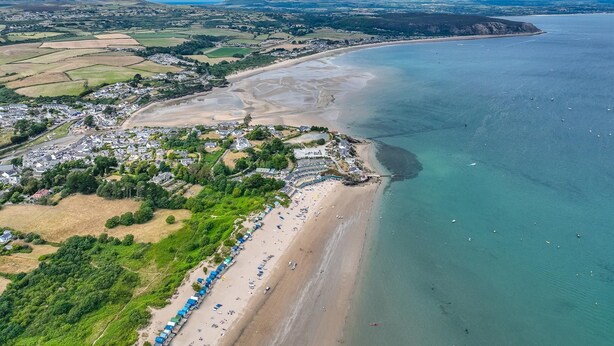 An aerial view of a coastal town with a beach, houses, and fields.