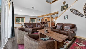 Ein geräumiges Wohnzimmer mit Ledersofas, einem Holztisch und einer Küche im Hintergrund.