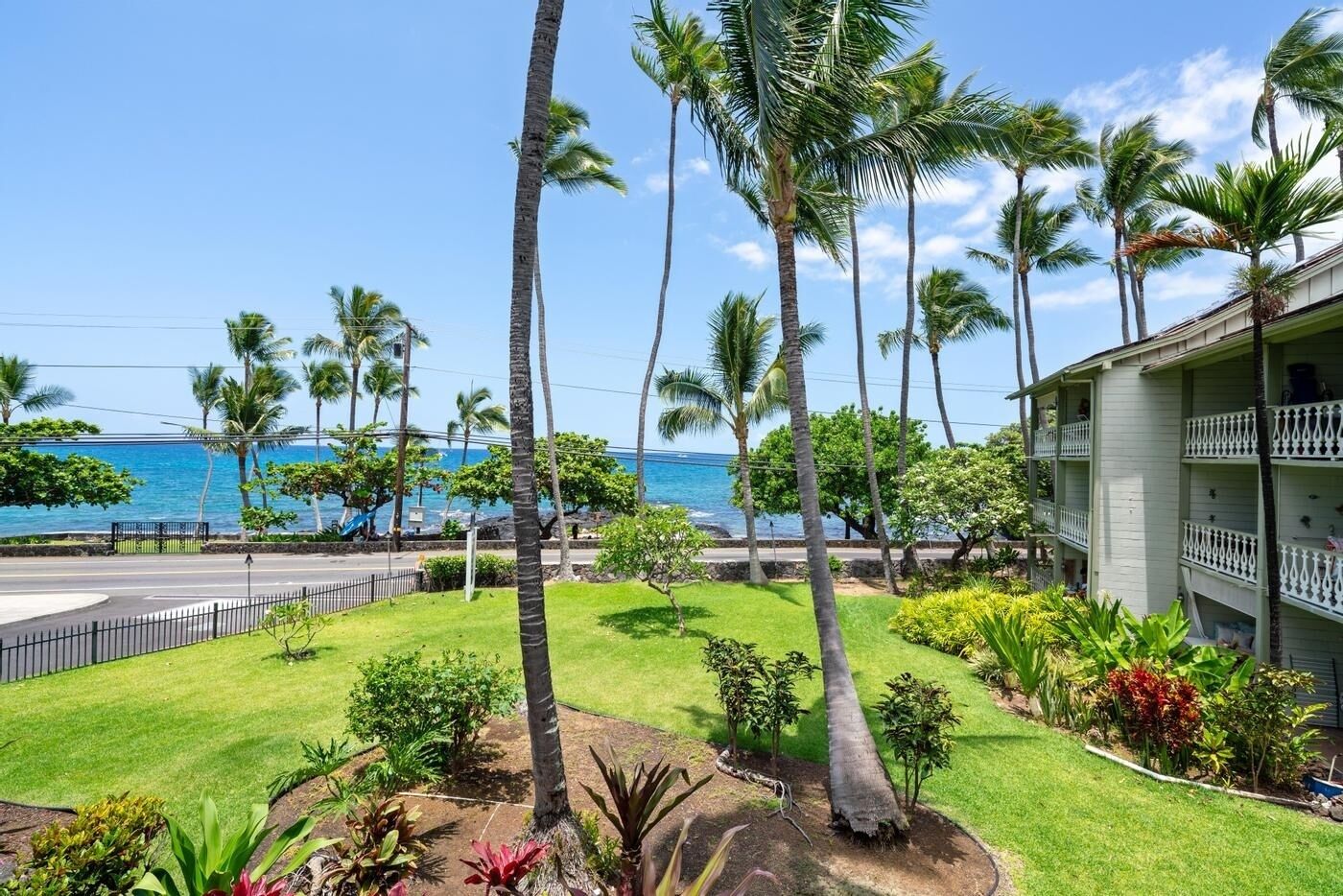 A hotel with a view of the ocean, surrounded by palm trees and a well-maintained lawn.