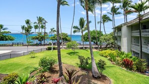 A hotel with a view of the ocean, surrounded by palm trees and a well-maintained lawn. - Big Island Kona Islander 245 Condo (Kailua-Kona)