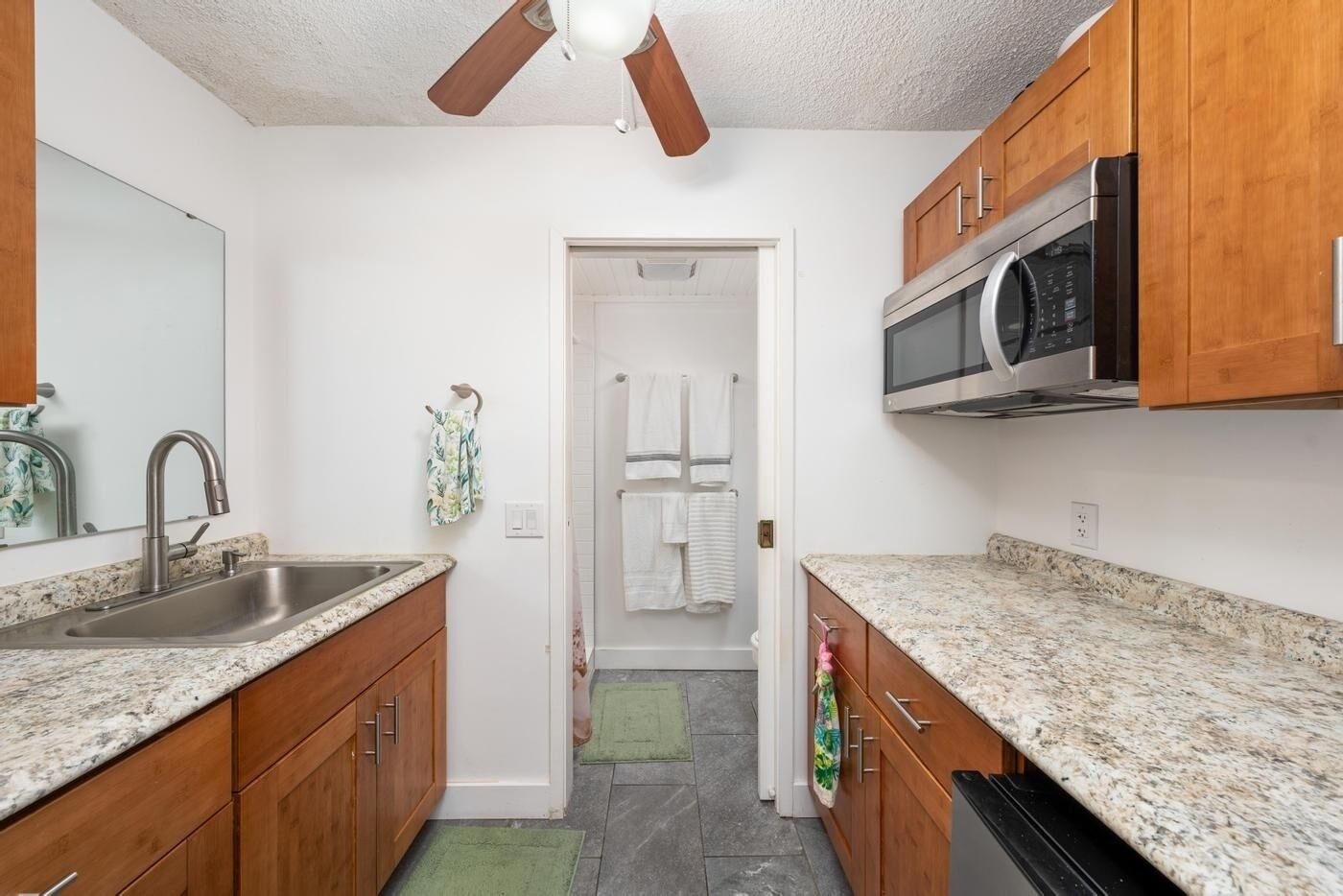 A kitchen with granite countertops, wooden cabinets, a stainless steel sink, a microwave, and a ceiling fan.