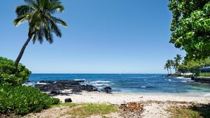 A beach with clear blue water, a sandy shore, and palm trees. - Big Island Kona Islander 245 Condo (Kailua-Kona)