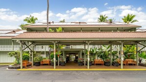 A two-story building with a covered entrance, outdoor seating, and tropical plants. - Big Island Kona Islander 245 Condo (Kailua-Kona)