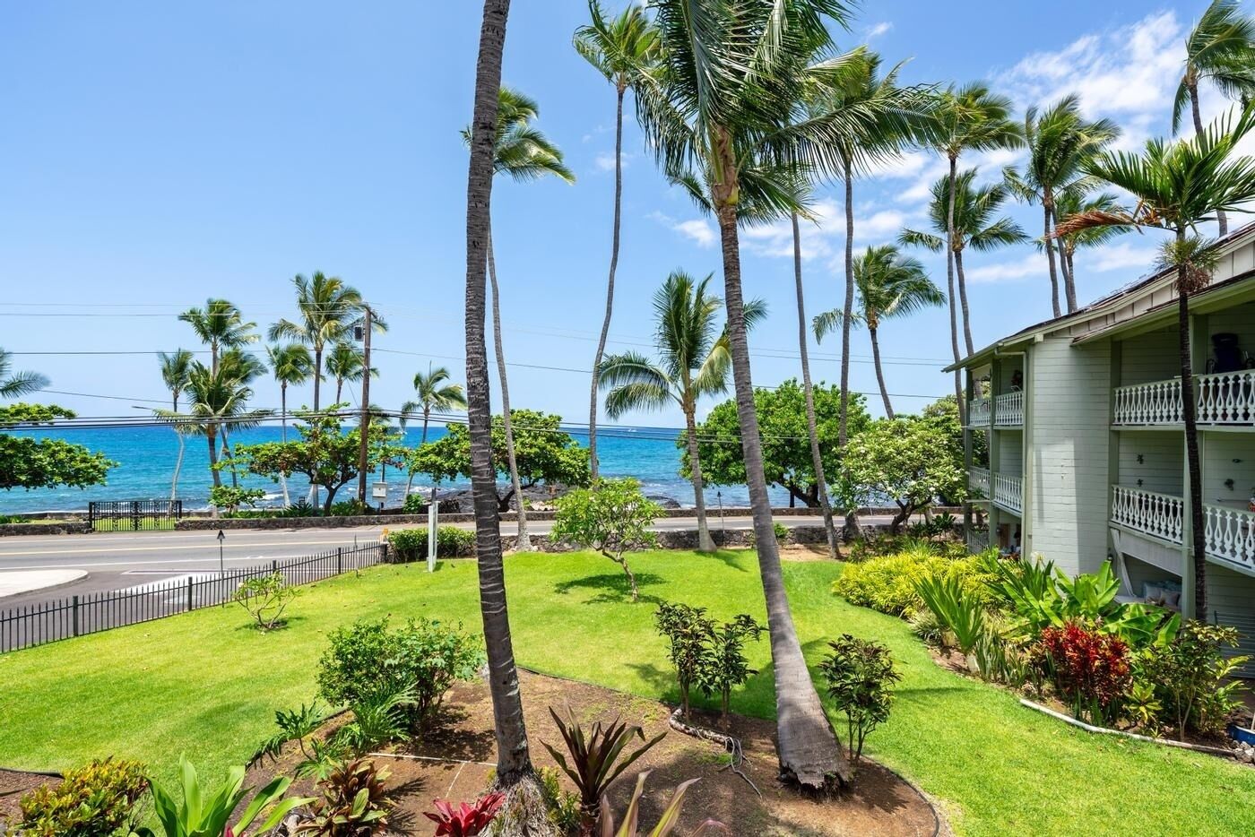 A hotel with a view of the ocean, surrounded by palm trees and a well-maintained lawn.