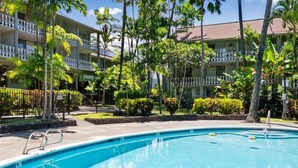 A swimming pool with a metal ladder, surrounded by palm trees and a multi-story building with balconies. - Big Island Kona Islander 245 Condo (Kailua-Kona)