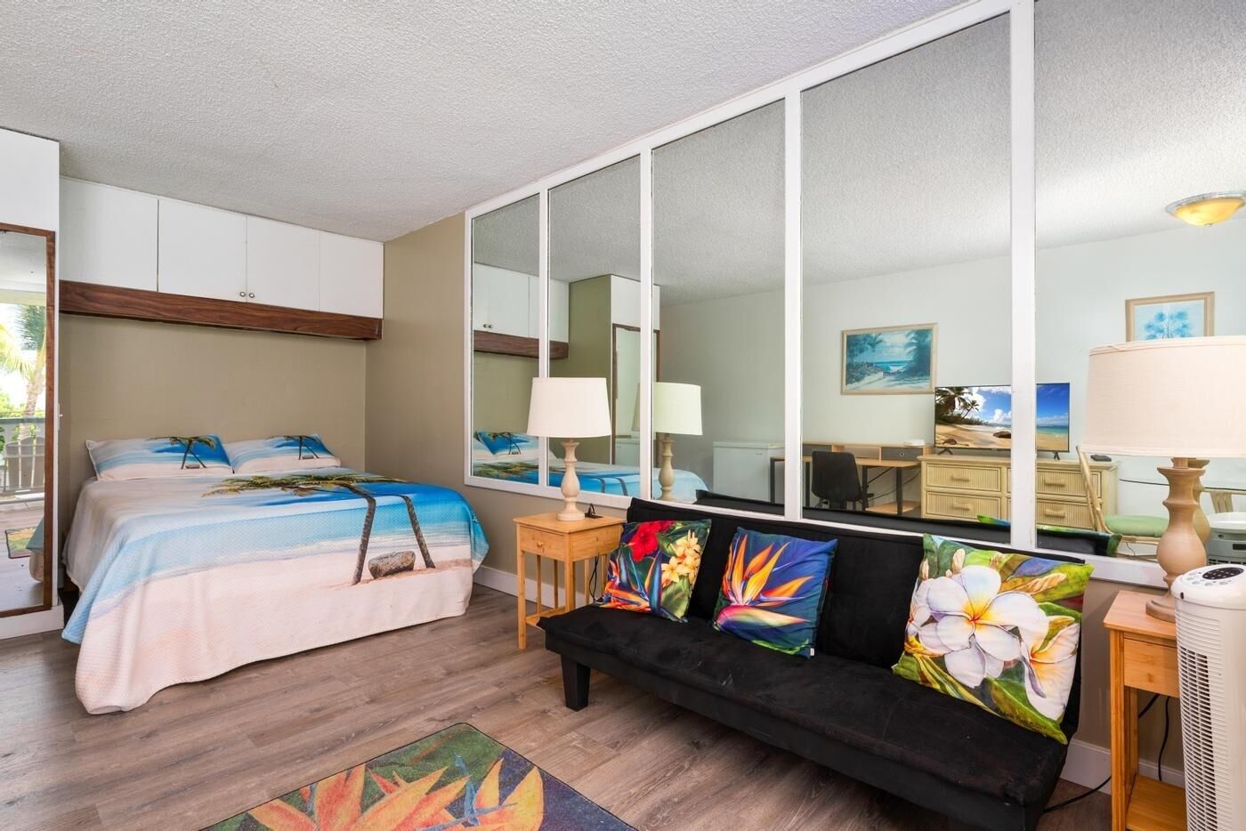 A bedroom with a bed, a sofa, a desk, and a large window.