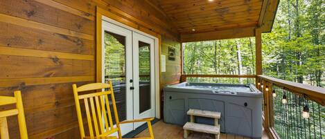 A wooden deck with a hot tub, a rocking chair, and a small table.