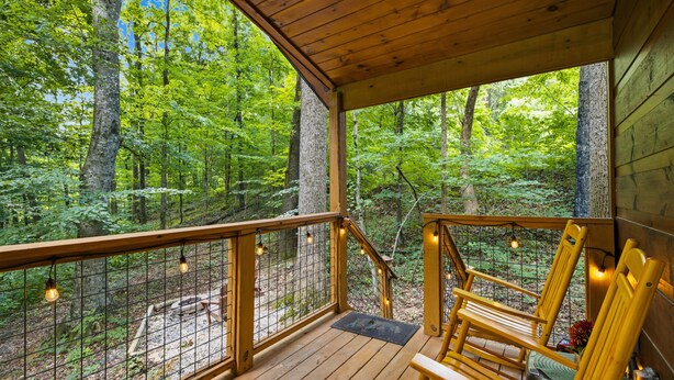 Una terraza de madera con barandilla, sillas de madera y vistas a un bosque.