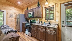 Interior de una cabaña de madera con cocina, que incluye refrigerador, estufa, microondas y lavamanos.