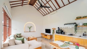 A modern living space with a sofa, dining table, TV, and kitchen area. - Villa w/ Pool, Rice Field & Mountain Views (Pererenan)