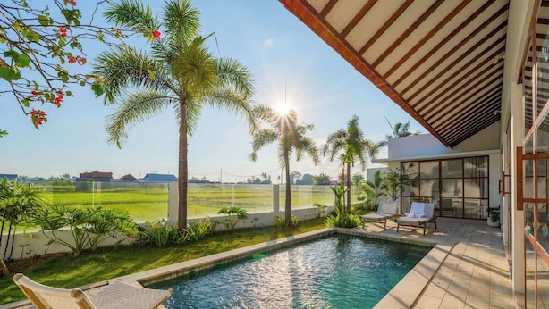 A swimming pool with a view of a field, surrounded by palm trees and a covered patio area. - Villa w/ Pool, Rice Field & Mountain Views (Pererenan)