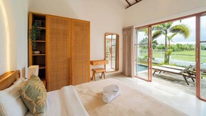 A hotel room with a bed, a desk, a wardrobe, and a large sliding glass door leading to a pool area. - Villa w/ Pool, Rice Field & Mountain Views (Pererenan)