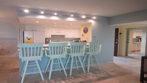 Una cocina moderna con armarios blancos, una isla central y una zona de comedor con sillas azul claro.