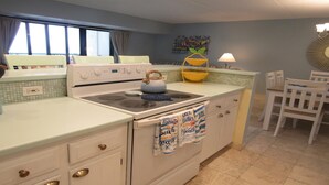 Una cocina con estufa, hervidor y comedor con sillas.