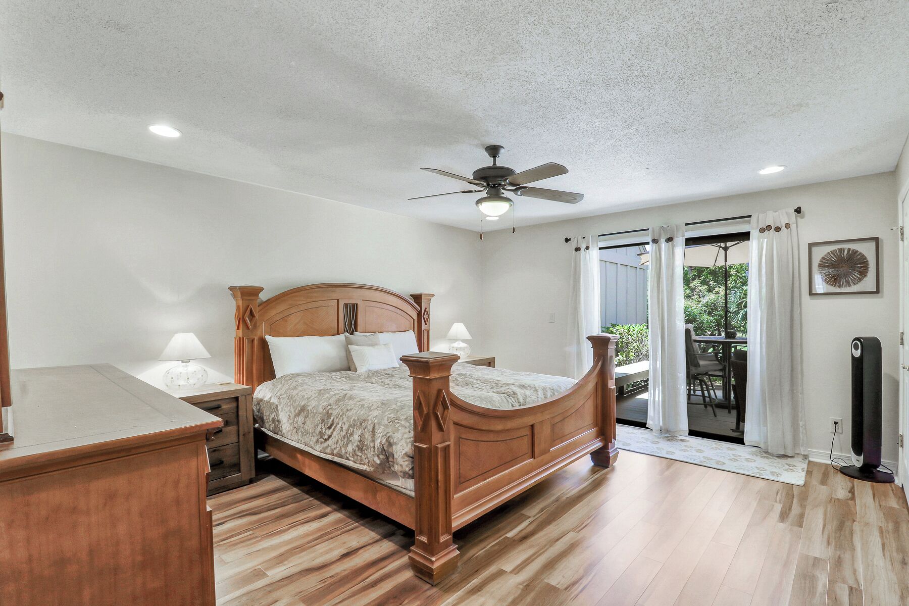 A bedroom with a wooden bed, a ceiling fan, and a view to an outdoor patio.