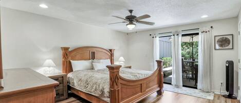 A bedroom with a wooden bed, a ceiling fan, and a view to an outdoor patio.