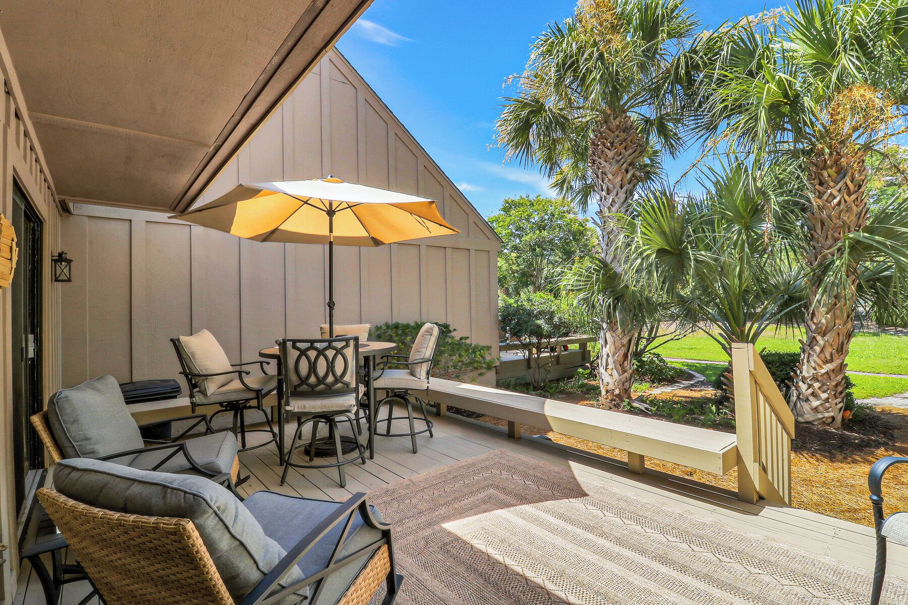 An outdoor patio area with a covered seating arrangement, including chairs and a table, and a large umbrella providing shade.