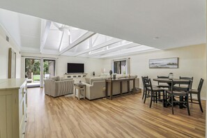 A spacious living area with a large flat-screen TV, a dining table with chairs, and a sofa set. - Sunset Rentals | Queens Grant 671 | Dog Friendly (Hilton Head Island)