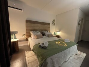 Quarto com cabeceira de madeira, colcha verde, roupa de cama branca e mesa de cabeceira com abajur.