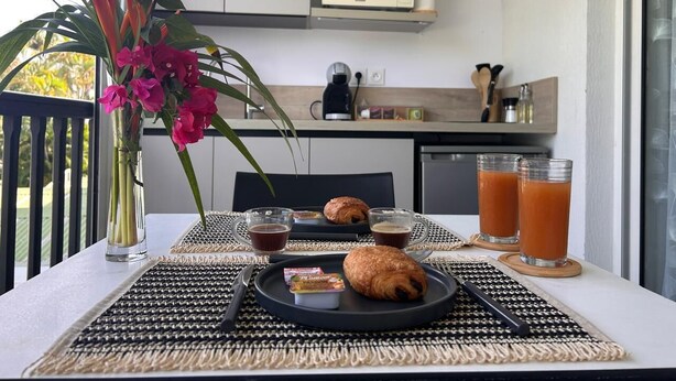 A breakfast setup with croissants, juice, and a flower vase on a balcony.