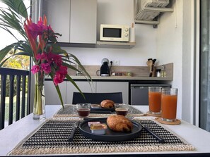 Mesa de café da manhã com croissants, suco e um vaso de flores numa varanda.