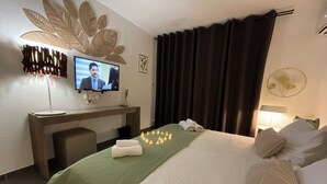 A hotel room with a bed, a desk with a computer, a TV, and a wall-mounted decorative leaf design.