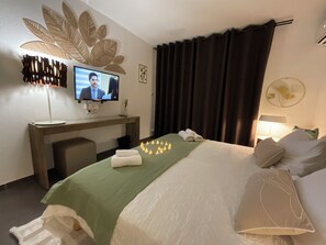 Une chambre d’hôtel comprenant un lit, un bureau avec un ordinateur, une télévision et un motif décoratif en forme de feuille fixé au mur.