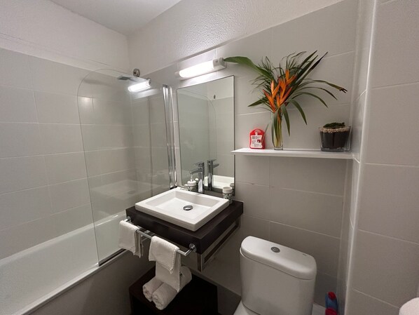 Uma casa de banho moderna com cabine de duche em vidro, uma sanita branca, uma pia e um espelho.