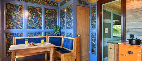 A room with a wooden ceiling, a bench, a table with breakfast items, and an orange stove.