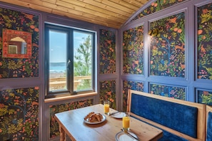 Ein Zimmer mit Holzboden, einem Fenster mit Aussicht, einem Tisch mit Frühstück und blumigem Wandpapier.