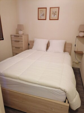 Ein Schlafzimmer mit einem hölzernen Bett, zwei Nachttischen mit Lampen, einer Kommode und zwei gerahmten Bildern an der Wand.