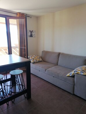 Ein Wohnzimmer mit einer Couch, einem Esstisch mit Hockern und einer Schiebetür aus Glas.
