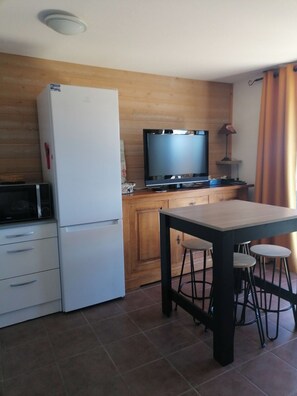 Eine Küche mit Kühlschrank, Mikrowelle und Fernseher auf einem Holzschrank. Ein Tisch mit Stühlen und einer Lampe steht ebenfalls dort.