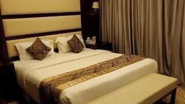 Une chambre d’hôtel avec un grand lit, une table de chevet, une commode et une moquette à motifs.